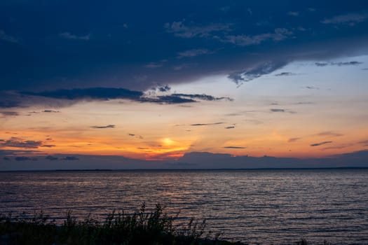 Stunning sunset over a calm sea, vivid colors in the sky with soft light reflecting on the water.