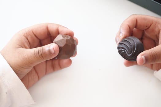Two hands grasp unique chocolate pieces inside a bright indoor setting.