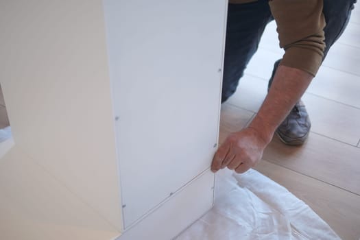 A person is assembling a white furniture piece in a bright room.