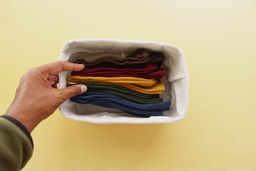 A hand arranges neatly folded socks in different colors in a basket.