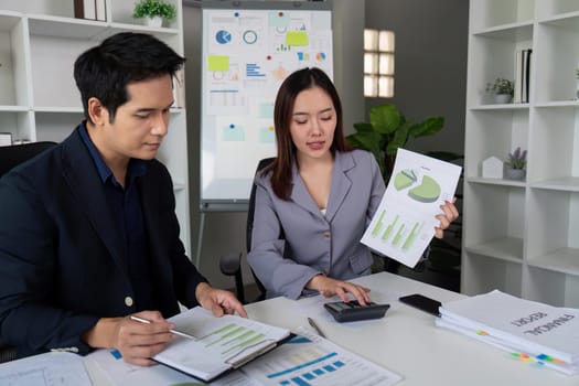 A focused meeting between two professionals, one presenting analytical charts while the other takes notes, symbolizing effective communication and analysis.