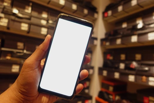 Person holds a blank smartphone inside a crowded shoe store.