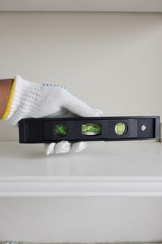 A hand wearing a glove holds a leveling tool to measure shelf balance.