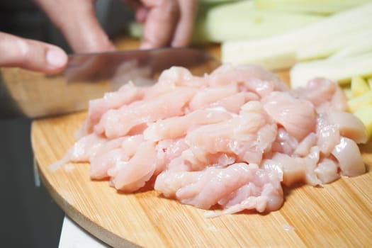 Chopping raw chicken on a wooden board alongside fresh celery stalks.