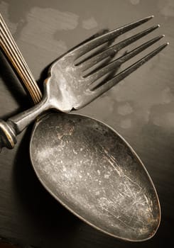Close-up of Ancient worn vintage cutlery on the dark background. Crossed black metal spoon and fork in dark tone, Highlighting its texture and design, use it as your Space for text, Design, Wallpaper and Poster, Selective focus.
