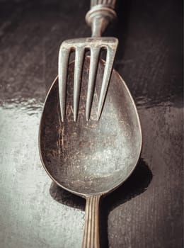 Close-up of Ancient worn vintage cutlery on the dark background. Crossed black metal spoon and fork in dark tone, Highlighting its texture and design, use it as your Space for text, Design, Wallpaper and Poster, Selective focus.