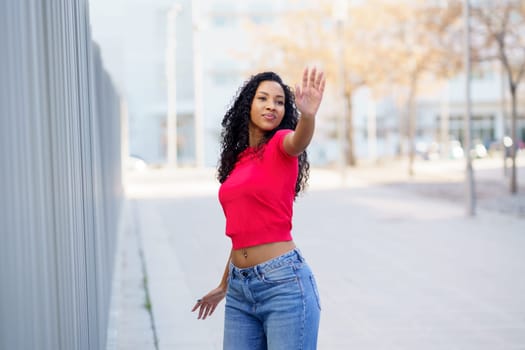 A stylish, confident young woman displays her unique fashion outdoors in a vibrant red top and trendy blue jeans, radiating positivity and inspiring others with her fun and free lifestyle