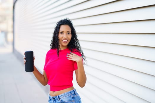 A confident woman wearing a vibrant pink crop top and stylish denim shorts poses joyfully with a refreshing drink in hand, radiating positivity and cheer against a modern and fashionable backdrop