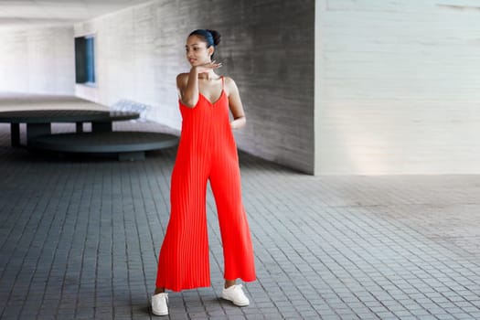 In an urban environment, a stylish and fashionable woman is striking a confident pose while wearing a vibrant red jumpsuit, effectively showcasing her contemporary sense of style and natural grace