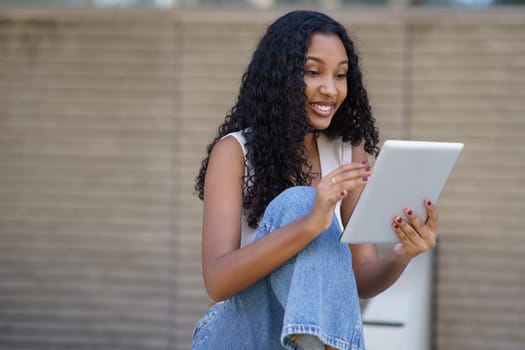 A cheerful and lively young woman is happily interacting with her tablet, effectively showcasing the significant role that technology plays in our daily lives, especially in an outdoor setting