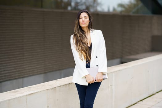 A stylish and confident businesswoman poses outdoors, dressed in a chic white blazer paired with trendy jeans, effectively showcasing a modern, professional look that embodies sophistication