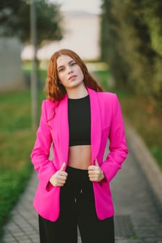 A confident and stylish young woman poses gracefully outdoors, showcasing her vibrant pink blazer that elegantly contrasts her chic black crop top, exuding an undeniable sense of style and attitude