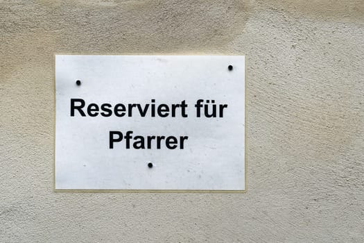 Sign in front of a church with the German inscription reserviert für Pfarrer. Translation: reserved for pastor