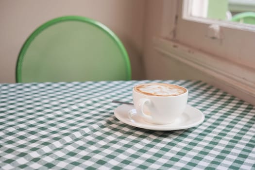 A cup of coffee sits on a round table with a green checkered cloth.