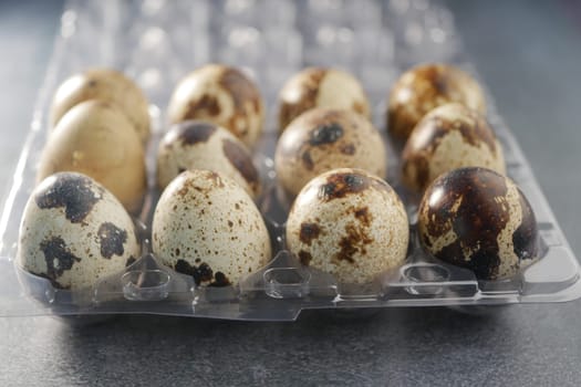 Different colored quail eggs are neatly placed in a plastic carton.