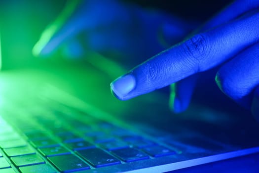 hacker typing on keyboard illuminated by green and blue light.