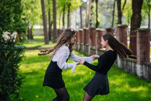 Two happy schoolgirls, dressed in black skirts, spinning joyfully while holding hands on a vibrant green schoolyard lawn