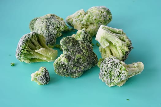 Several frozen broccoli florets scattered on a bright blue surface.