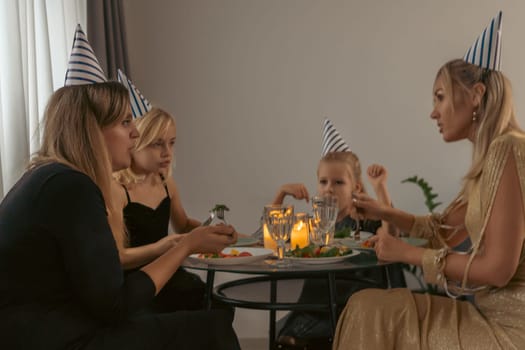 Four women and a child, wearing party hats, sit around a table with food and candles, celebrating a birthday.