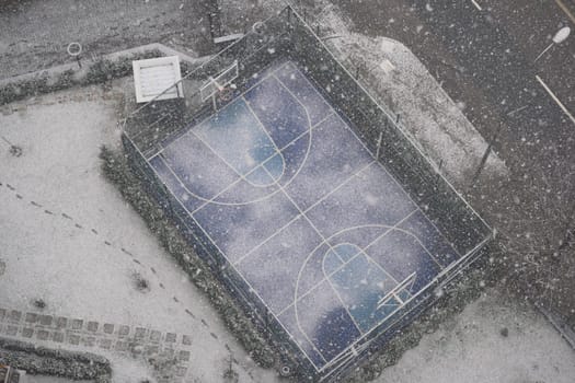 A basketball court is blanketed in snow under falling flakes.