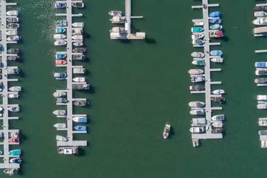 A boat is in the water near a marina with many other boats. The marina is full of boats of all sizes and colors