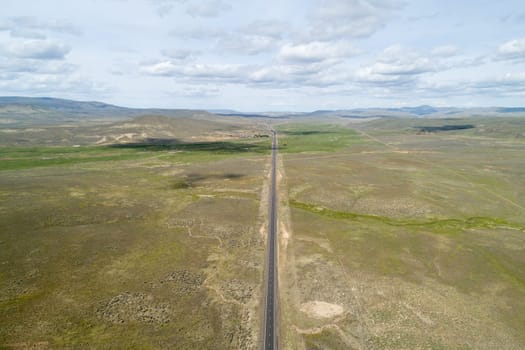 A long road stretches across a dry, barren landscape. The sky is cloudy, and the sun is barely visible. The emptiness of the scene gives off a sense of loneliness and isolation