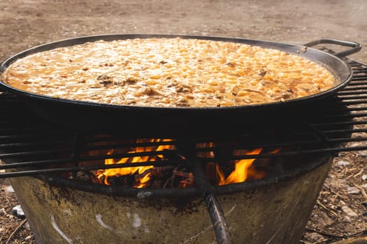 A large paella cooking over fire with a smokey background, at a street food festival