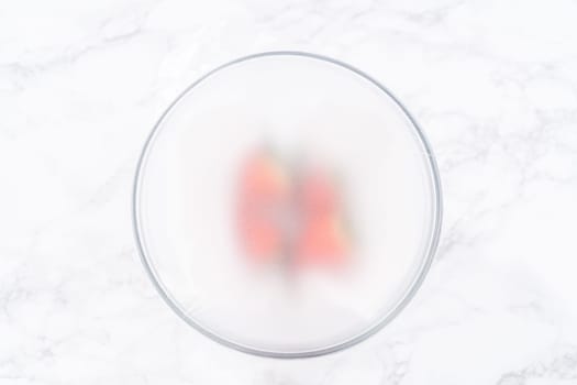 Strawberries, freshly washed and dried, are neatly stored in a glass bowl lined with a paper towel and securely covered with plastic wrap to maintain freshness.