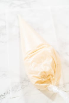 A single piping bag filled with white royal icing resting on a marble surface, ready for decorating festive mitten cookies.