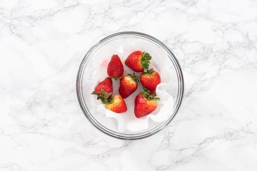 Freshly washed and dried strawberries are carefully arranged in a glass bowl lined with paper towel, ready for snacking or further use.