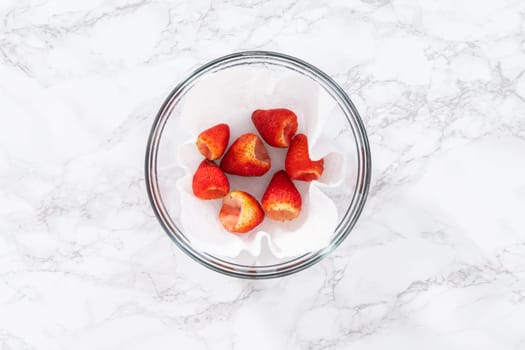 Freshly washed and dried strawberries are carefully arranged in a glass bowl lined with paper towel, ready for snacking or further use.