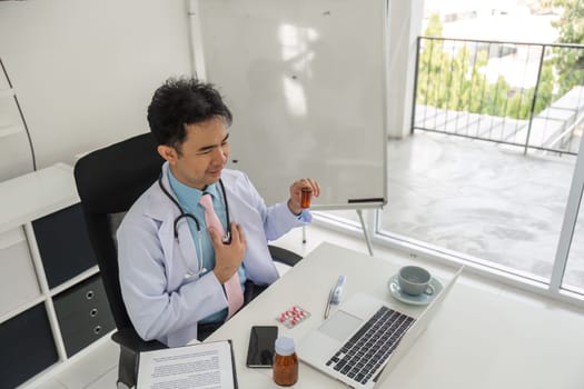 During a video call with a patient, a physician thoughtfully examines medications, ensuring tailored healthcare solutions in a spacious office environment.