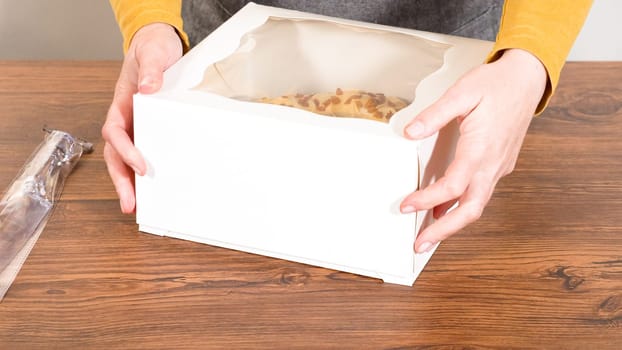 Carefully placing the gingerbread bundt cake, adorned with salted caramel frosting and gingerbread sprinkles, into a white paper bundt cake box with a clear window for gifting.