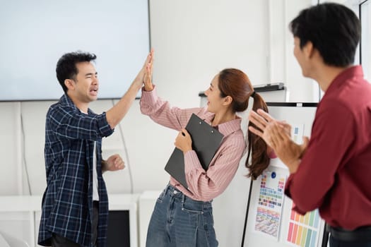 In a vibrant office setting, two colleagues enthusiastically high-five each other while a third team member shares in the joyful moment, showcasing teamwork and camaraderie.