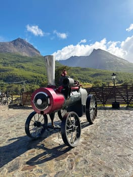 Vintage red and black steam engine displayed outdoors with scenic green mountains and blue sky in Ushuaia, Argentina.