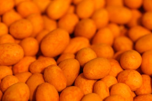 A multitude of bright orange candies fills the space, their glossy surfaces reflecting gentle light as shoppers browse in a lively market. The sweet aroma fills the air, enticing all who pass by.
