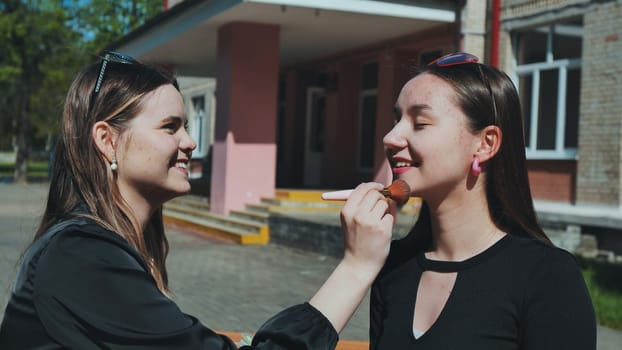 Two teenage girls having fun applying makeup during a school break, enjoying their time together outside