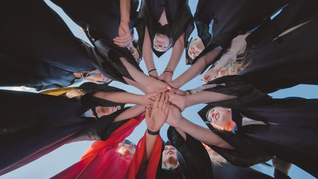 Recent graduates in their robes come together to celebrate their academic success by joining hands