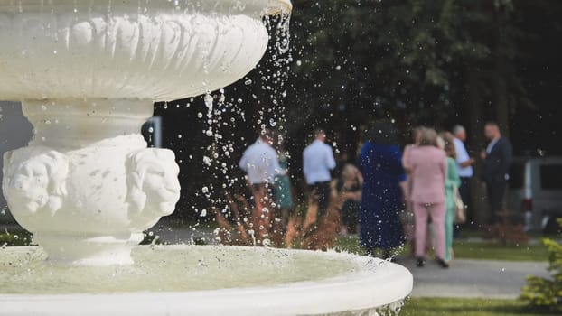 White fountain cascading water, blurred wedding guests celebrating, elegant scene capturing festive moment with soft, serene background ambiance