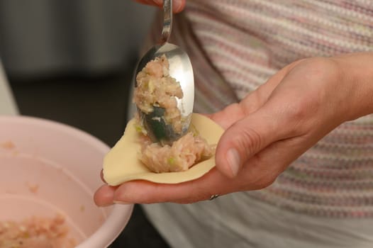 Hands skillfully shape homemade dumplings filled with savory meat mixture. The warm kitchen environment highlights creativity and culinary tradition during a leisurely weekend.