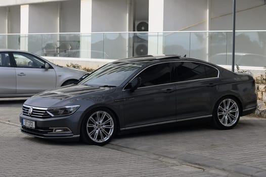 A stylish gray sedan rests on a patterned pavement near a contemporary structure, basking in the ambient warmth of day. The car's glossy finish reflects its surroundings, capturing attention.