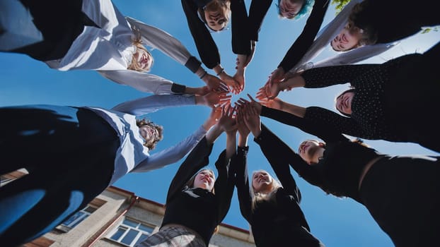 Group of students forming a circle, joining hands together in unity and teamwork, celebrating a successful school day achievement against a clear blue sky