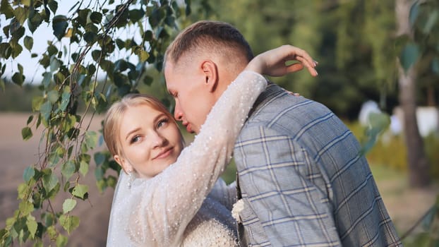 Newlyweds embracing tenderly beneath birch tree, wedding attire gleaming, radiating intimate joy and romantic connection