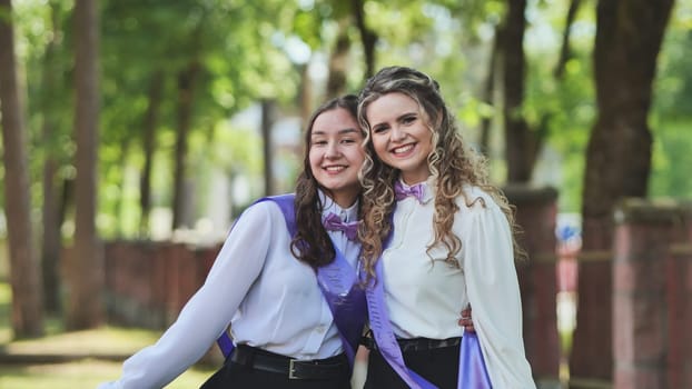 Two recent female graduates embracing on their last day of school, exuding joy in a beautiful green park. Embracing their success, eagerly anticipating what lies ahead