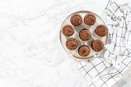Flat lay. Freshly baked cupcakes have been masterfully infused with rich caramel and adorned with velvety chocolate frosting, all elegantly presented on a pristine white serving plate.