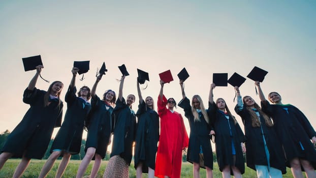 Group of smiling graduates raising mortarboards in celebration of academic achievement at sunset