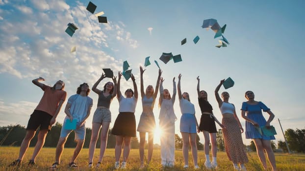Group of cheerful students throwing notebooks in the air celebrating the end of school at sunset