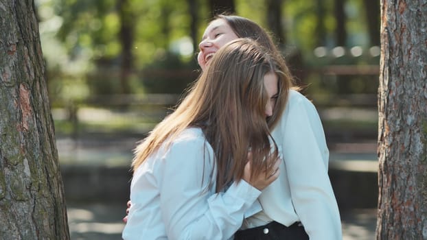 Two female friends sharing a tender moment, laughing and hugging in a park, enjoying their time together
