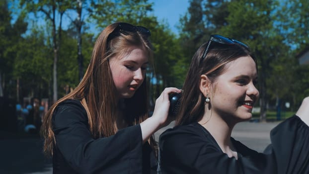 Two girls happily brushing their hair together in a sunny schoolyard, savoring a carefree moment amidst a bustling school day