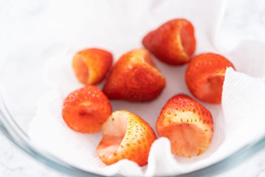 Freshly washed and dried strawberries are carefully arranged in a glass bowl lined with paper towel, ready for snacking or further use.
